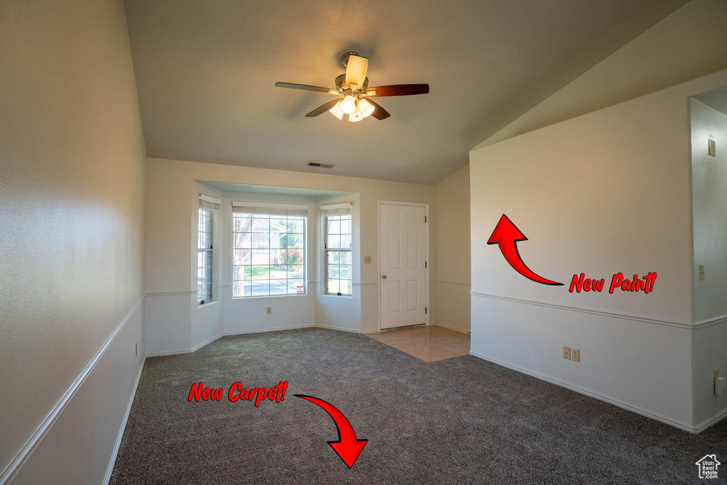 Carpeted empty room featuring lofted ceiling, baseboards, visible vents, and ceiling fan