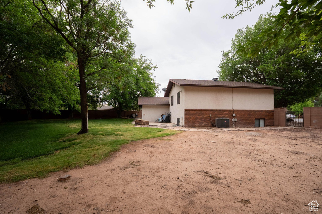 Rear view of property with a gate, fence, brick siding, central AC, and a lawn