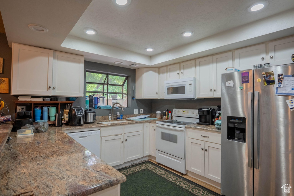 Kitchen with a tray ceiling, white appliances, a sink, and recessed lighting