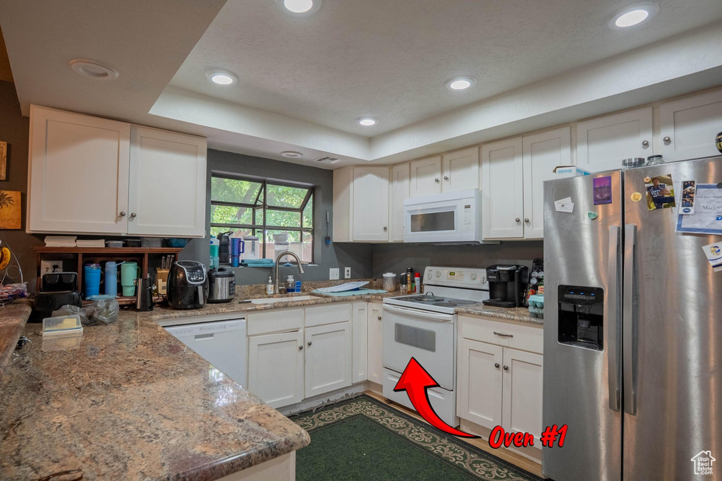 Kitchen with a sink, white appliances, a tray ceiling, and recessed lighting