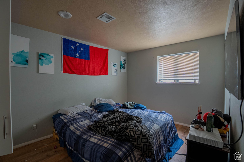 Bedroom with wood finished floors, visible vents, baseboards, and a textured ceiling
