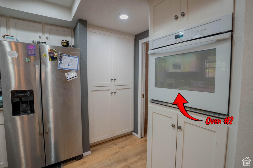 Kitchen featuring oven, light wood-style flooring, white cabinetry, and stainless steel fridge with ice dispenser