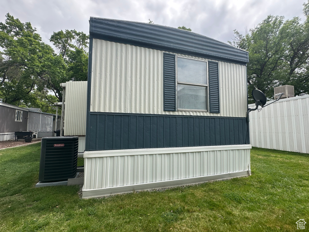 View of side of property with cooling unit, fence, and a lawn