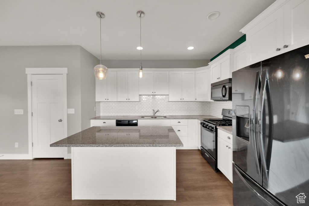 Kitchen featuring dark wood-style floors, a center island, black appliances, and stone countertops