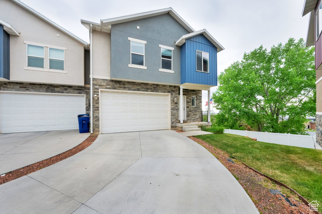 View of front facade featuring stone siding, a garage, stucco siding, a front yard, and driveway
