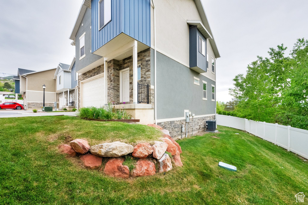 View of side of home with stone siding, an attached garage, fence, a yard, and driveway