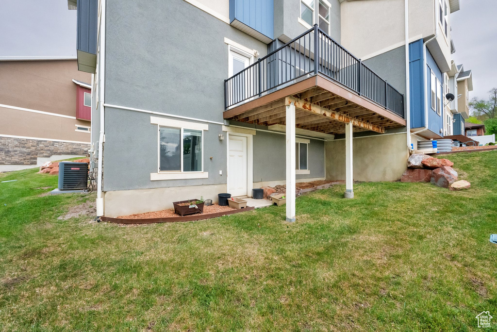 Back of property featuring a yard, stucco siding, central AC, and a wooden deck