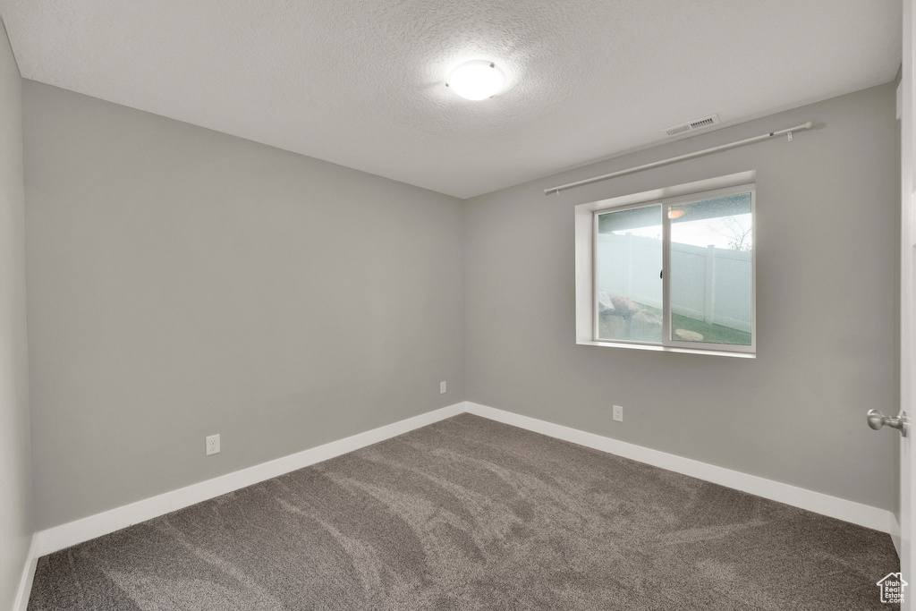 Spare room featuring baseboards, dark carpet, visible vents, and a textured ceiling