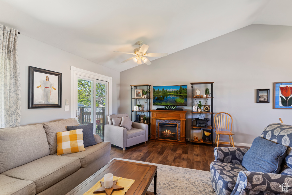Living area featuring vaulted ceiling, a warm lit fireplace, a ceiling fan, and dark wood-type flooring