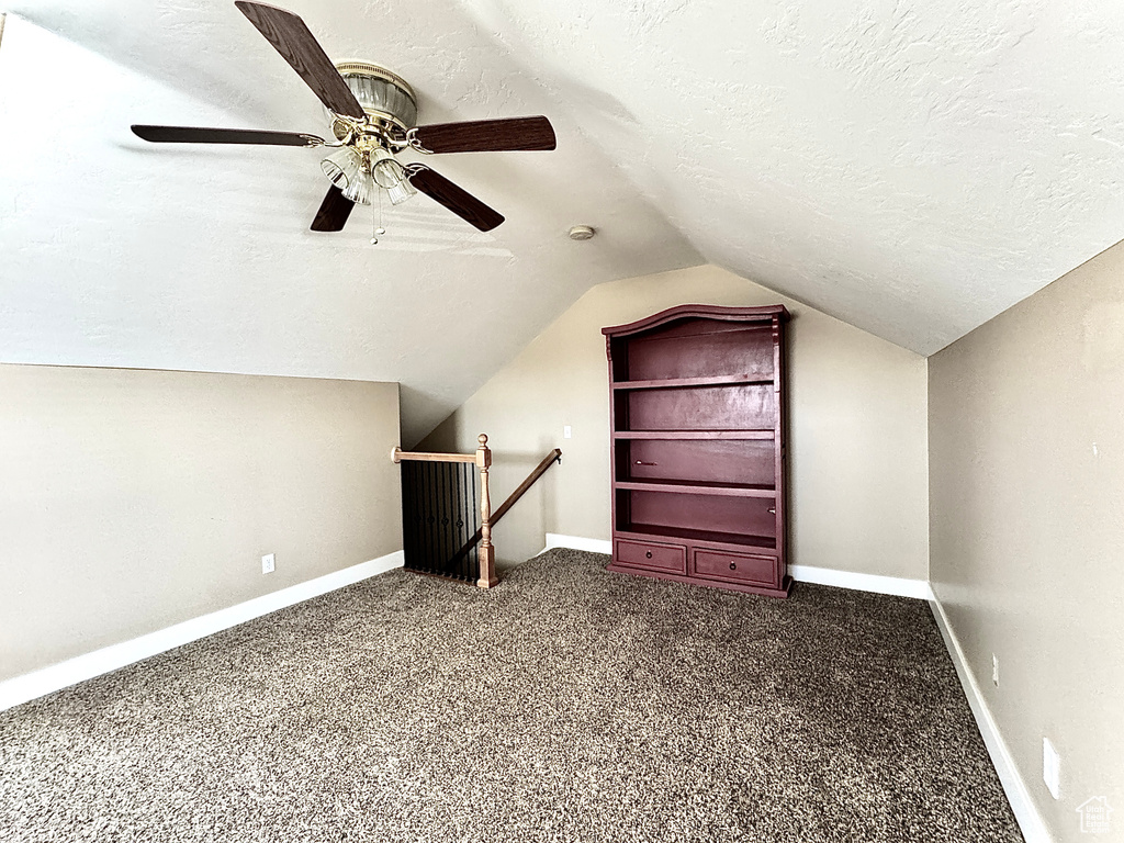 Additional living space with baseboards, dark carpet, a textured ceiling, and vaulted ceiling