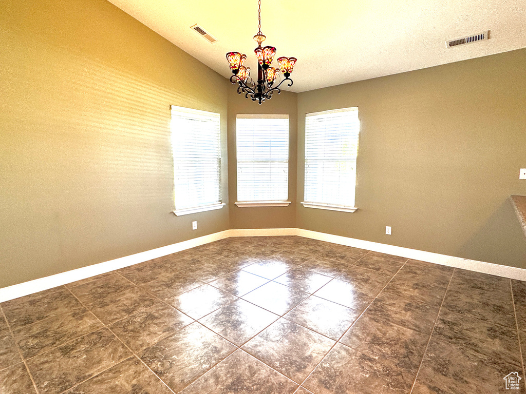 Empty room featuring an inviting chandelier, dark tile patterned flooring, baseboards, and visible vents