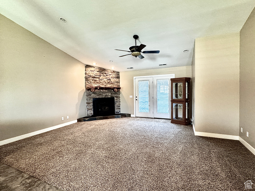 Unfurnished living room with baseboards, a stone fireplace, ceiling fan, and carpet