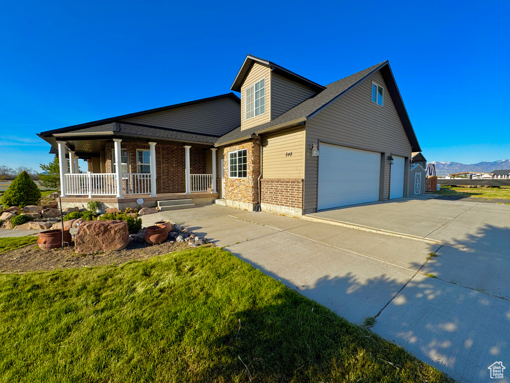 View of front of house with driveway, brick siding, a mountain view, covered porch, and roof with shingles