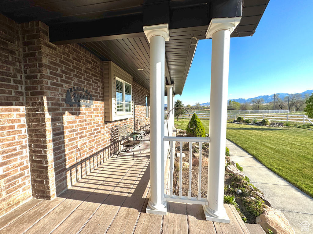 Wooden terrace featuring a porch, a mountain view, and a lawn