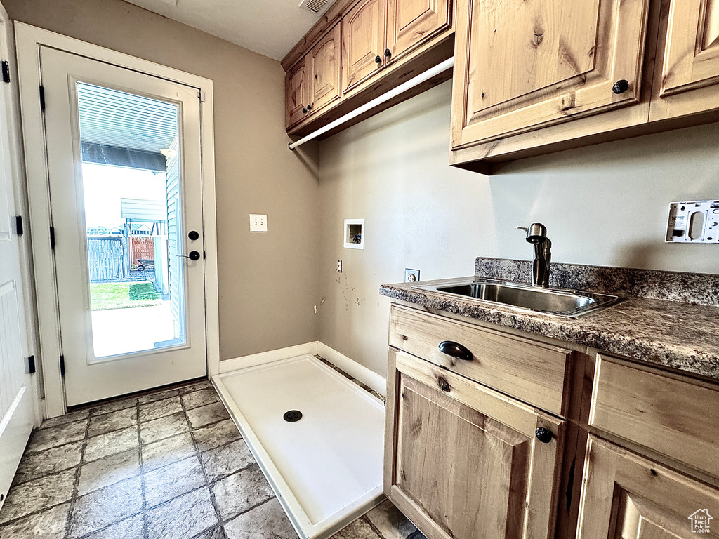 Washroom with cabinet space, stone tile flooring, hookup for a washing machine, and a sink