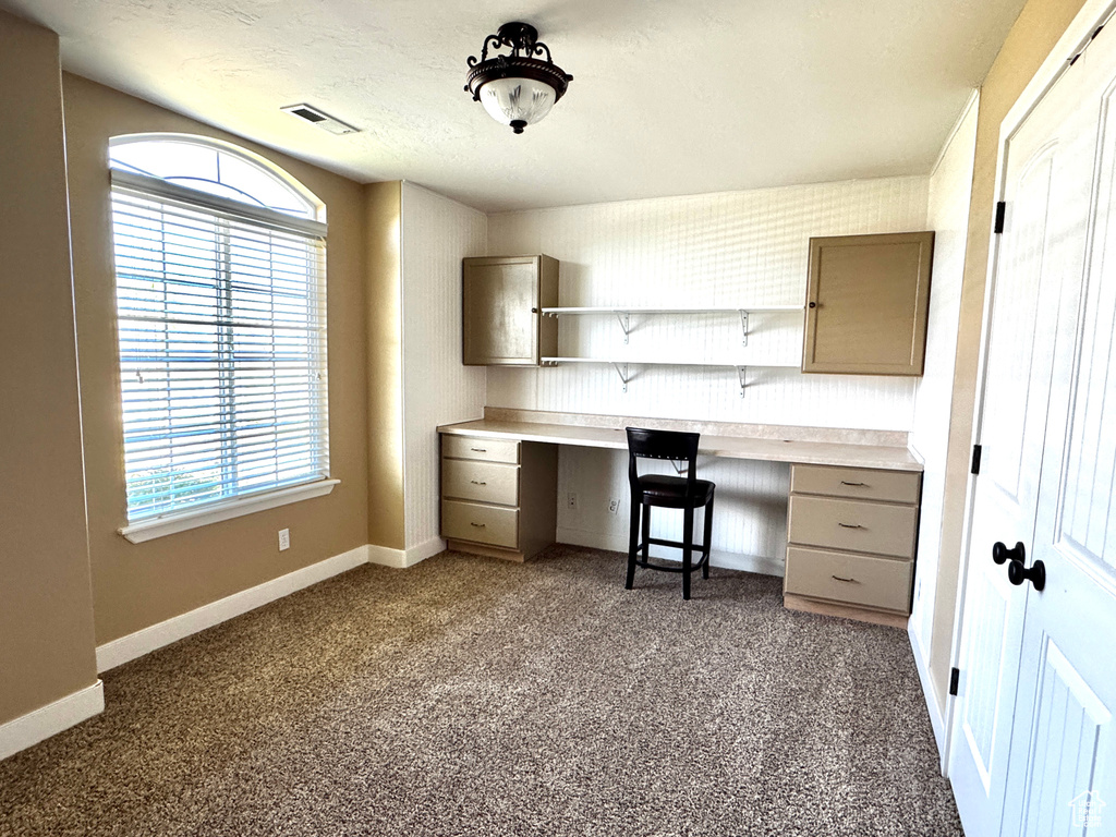 Unfurnished office with built in desk, dark colored carpet, baseboards, and visible vents