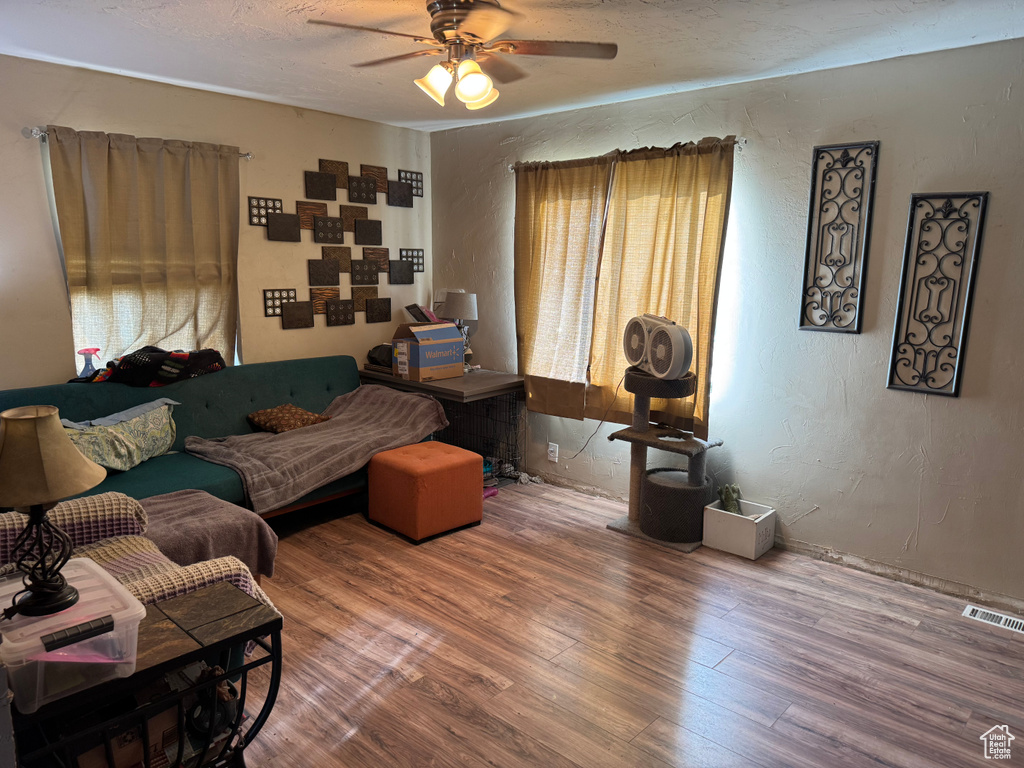 Living room with a textured wall, a ceiling fan, wood finished floors, and visible vents