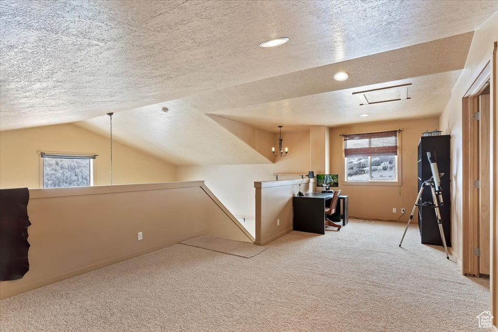 Unfurnished office featuring a textured ceiling, a notable chandelier, carpet, and vaulted ceiling