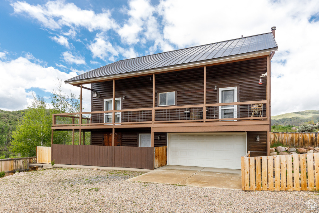 View of front of house featuring an attached garage, driveway, metal roof, and a balcony