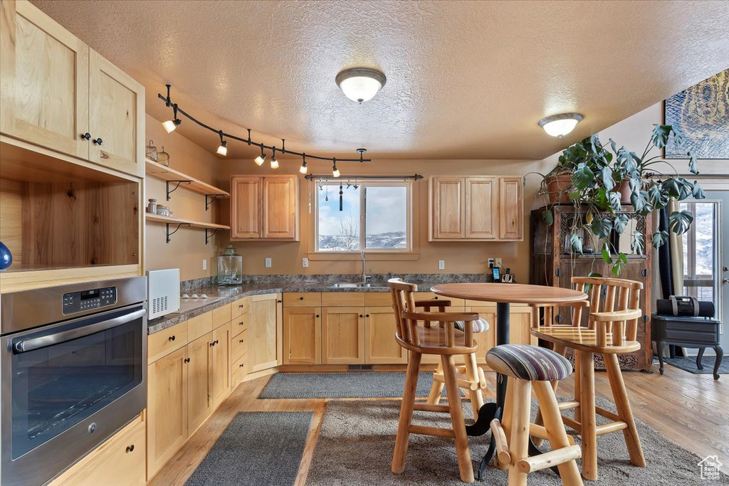 Kitchen featuring oven, a textured ceiling, light brown cabinetry, and light wood finished floors