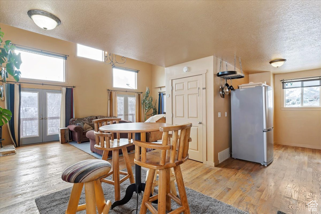 Dining space featuring a textured ceiling, visible vents, french doors, and light wood-style flooring