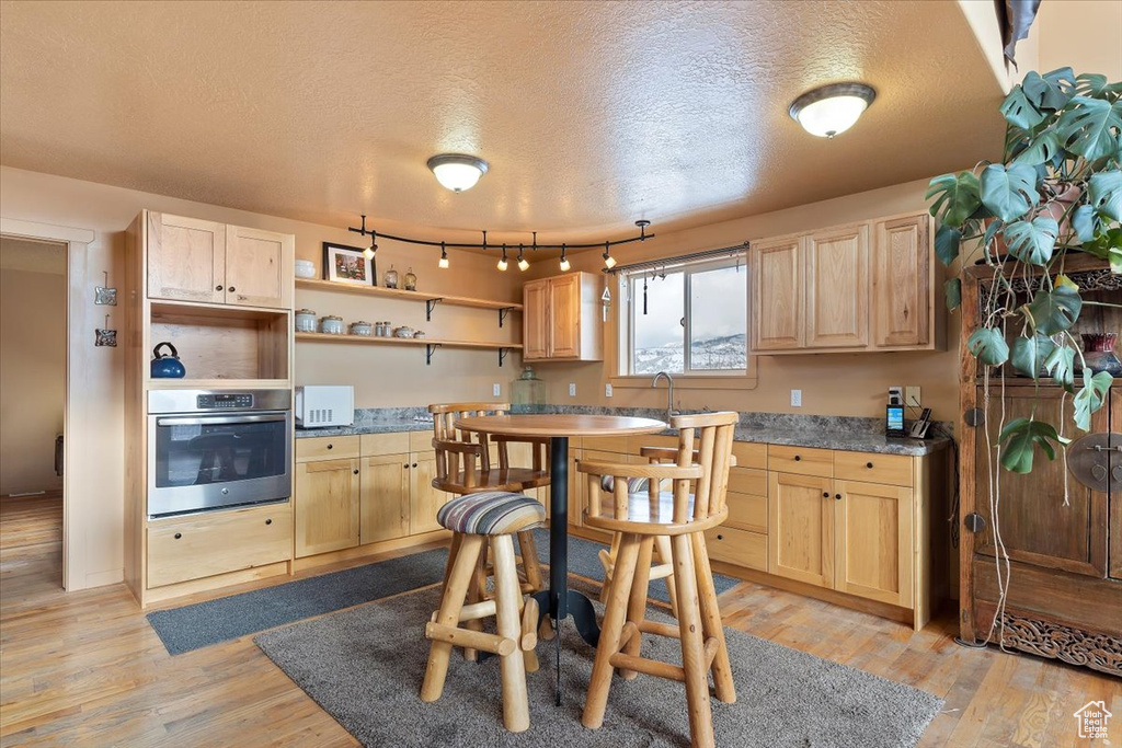 Kitchen with a textured ceiling, light brown cabinets, open shelves, and oven