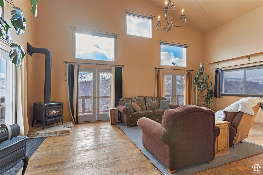 Living room with a notable chandelier, french doors, high vaulted ceiling, wood finished floors, and a wood stove