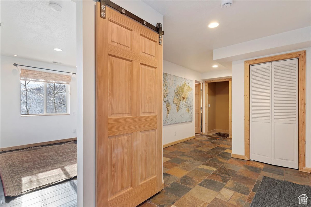 Hallway featuring baseboards, recessed lighting, a barn door, and stone finish floor
