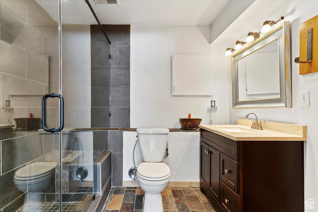 Full bathroom featuring vanity, toilet, a shower stall, and stone tile floors