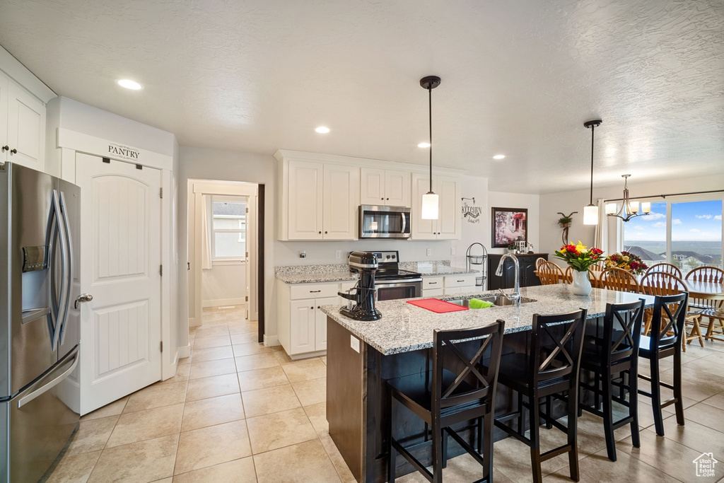 Kitchen featuring a kitchen bar, white cabinetry, light stone counters, a sink, and stainless steel appliances