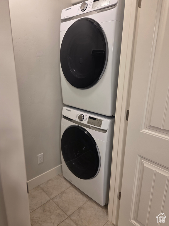 Laundry area featuring stacked washing machine and dryer, light tile patterned floors, and baseboards