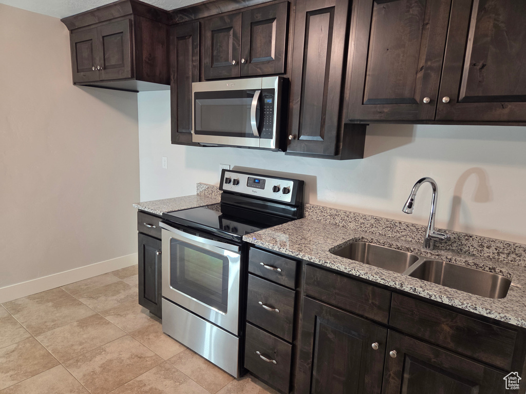 Kitchen featuring stainless steel appliances, a sink, baseboards, and light stone countertops