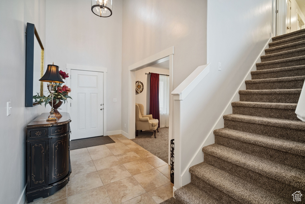 Foyer entrance with a towering ceiling, light tile patterned floors, baseboards, a notable chandelier, and stairs