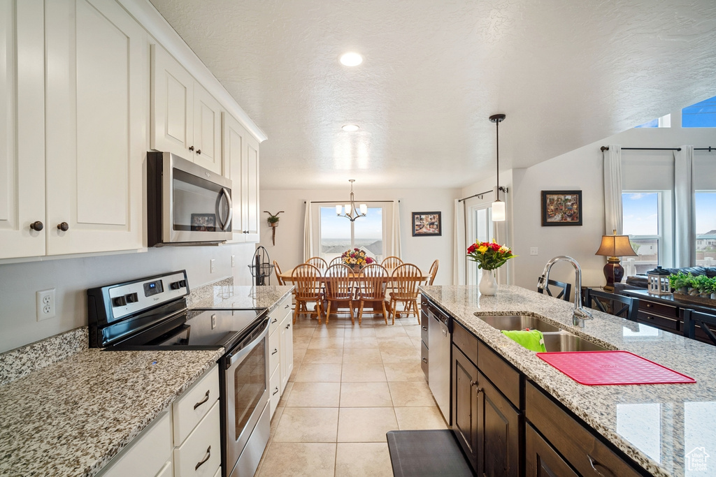 Kitchen featuring pendant lighting, appliances with stainless steel finishes, a sink, white cabinets, and a chandelier