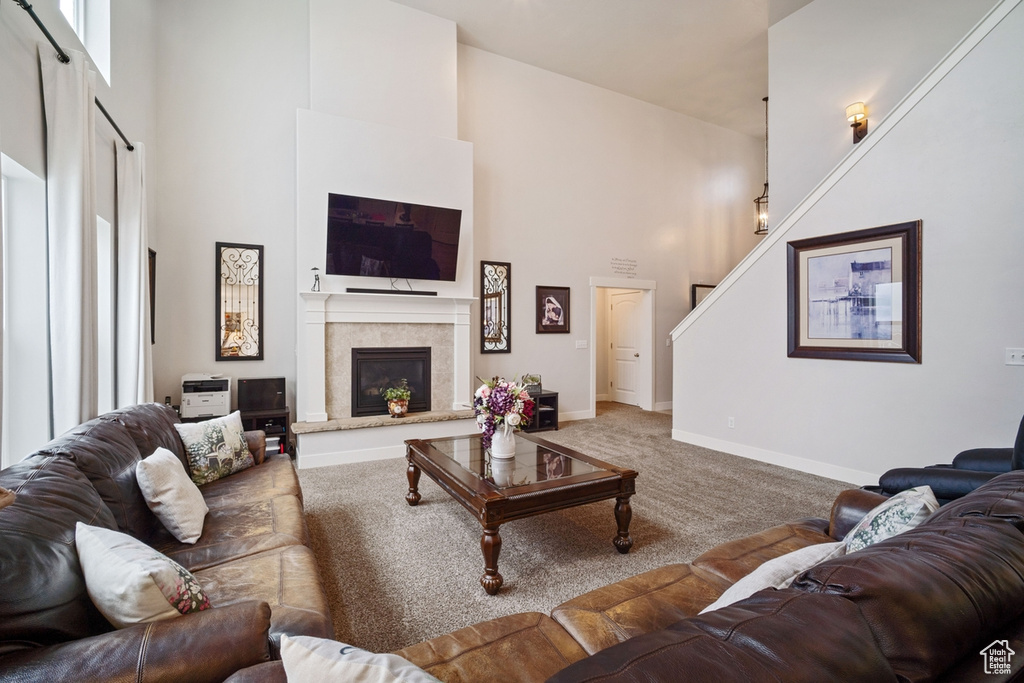 Carpeted living area featuring stairway, baseboards, a high ceiling, and a glass covered fireplace