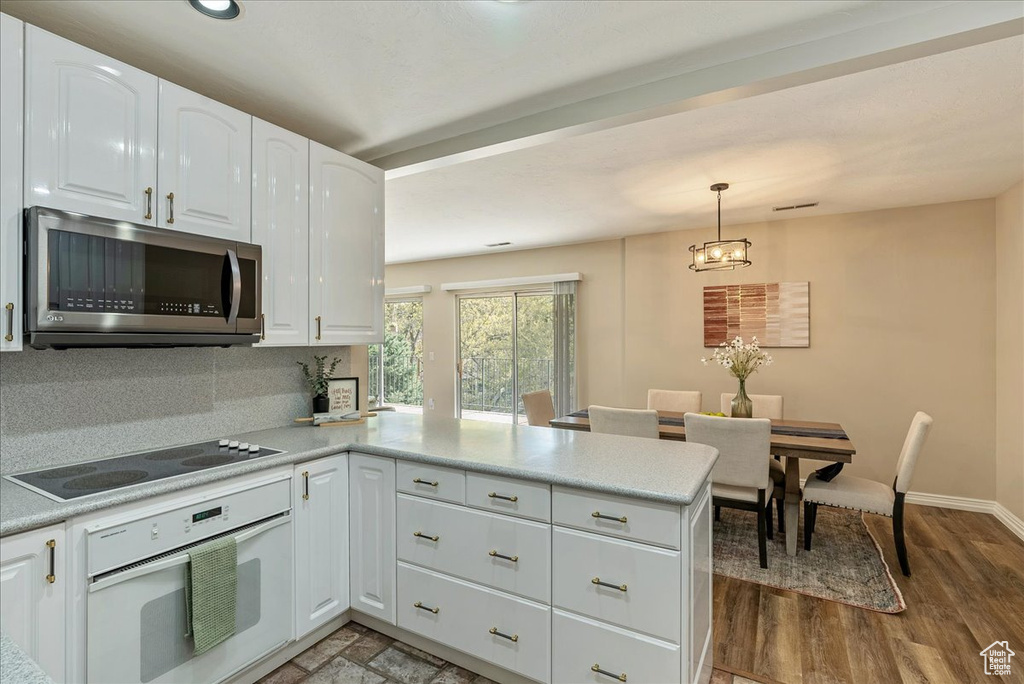 Kitchen with a peninsula, oven, white cabinets, stainless steel microwave, and black electric cooktop