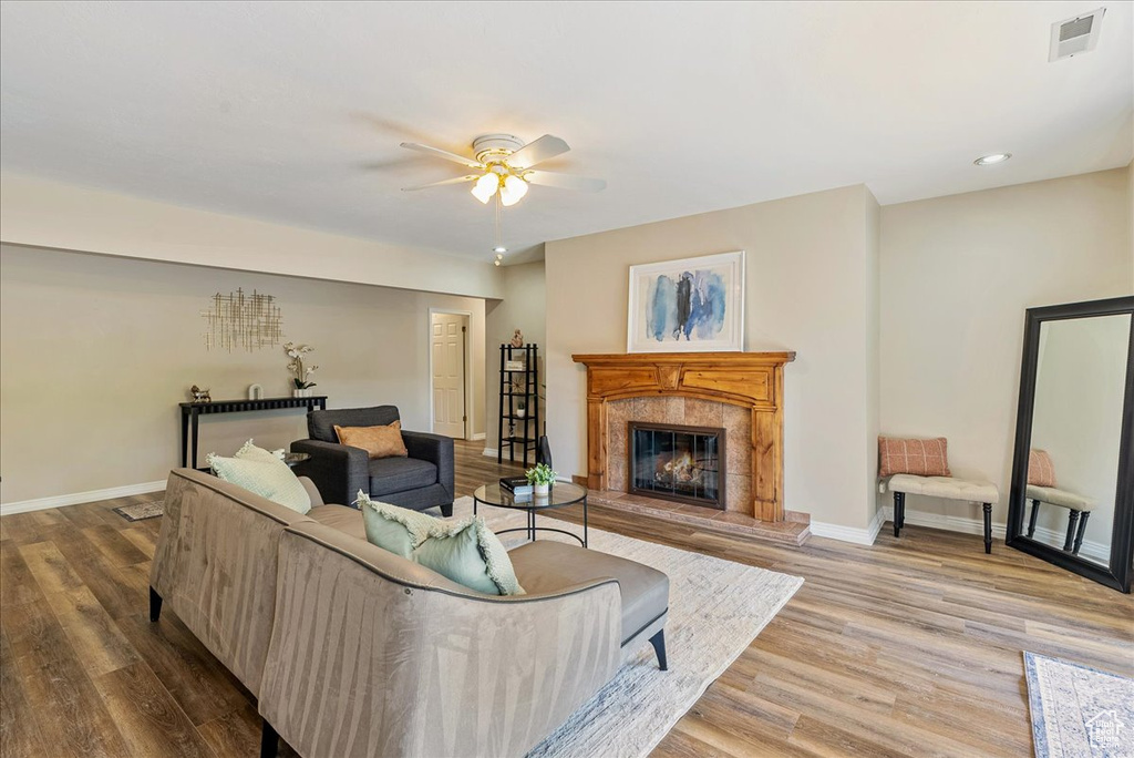 Living room with a ceiling fan, baseboards, a fireplace, and wood finished floors
