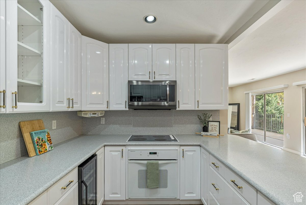 Kitchen featuring wine cooler, stainless steel microwave, black electric stovetop, white cabinets, and oven