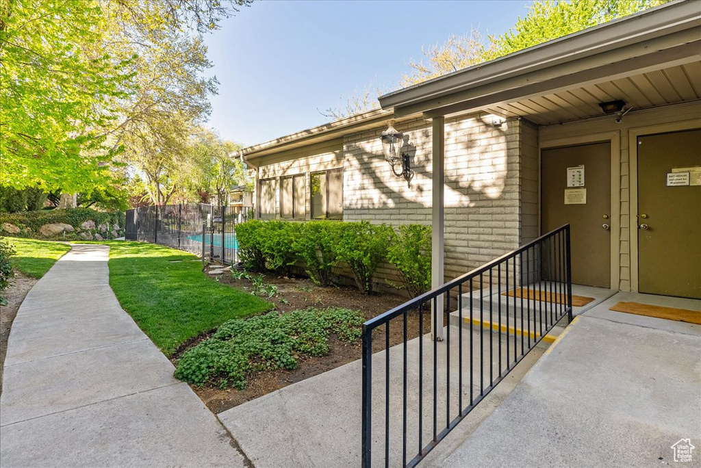 View of exterior entry featuring fence, a fenced in pool, brick siding, and a lawn