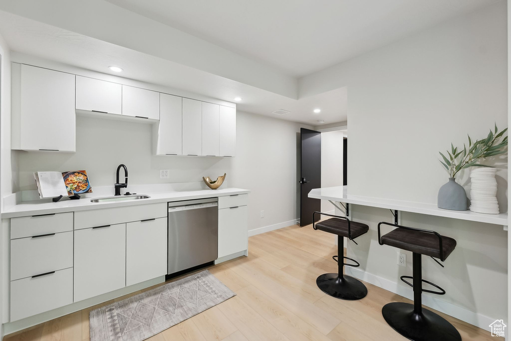 Kitchen with light wood finished floors, a sink, white cabinetry, stainless steel dishwasher, and baseboards