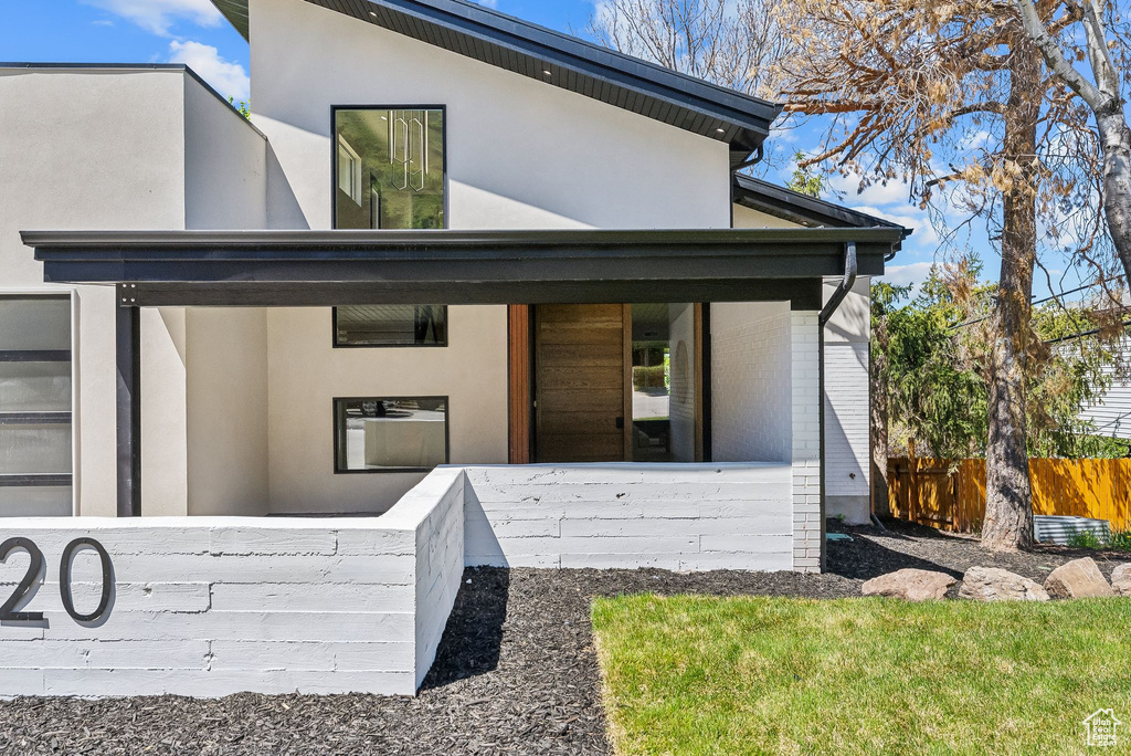 View of exterior entry with stucco siding, brick siding, and fence
