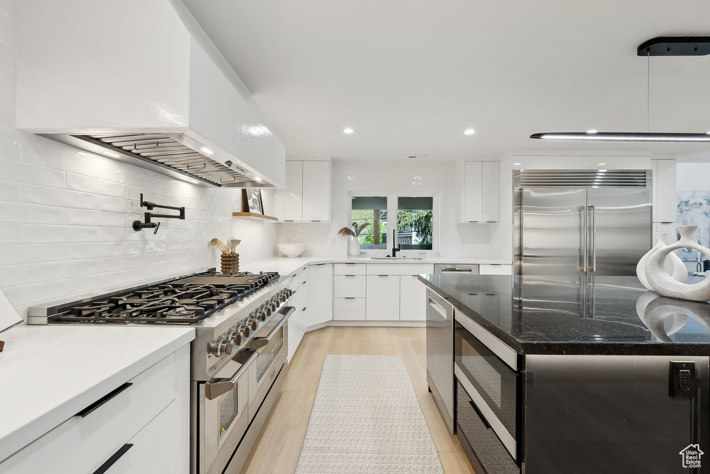 Kitchen featuring built in appliances, backsplash, white cabinetry, custom range hood, and modern cabinets