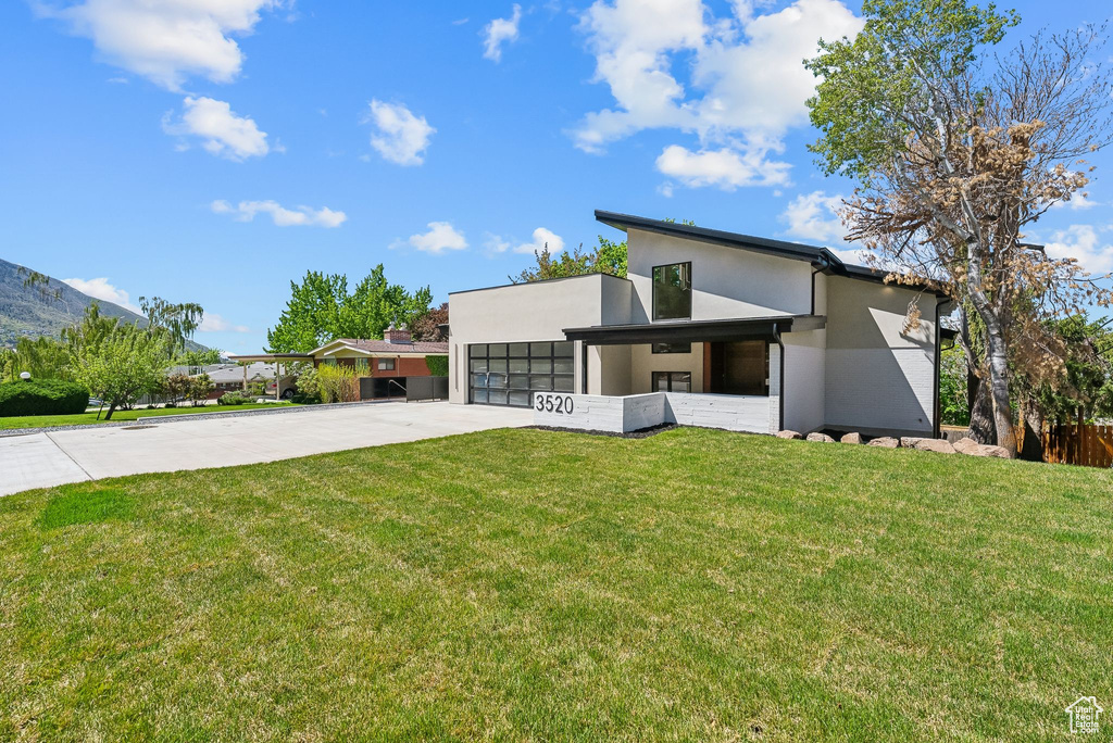 Contemporary home featuring concrete driveway, stucco siding, an attached garage, and a front yard