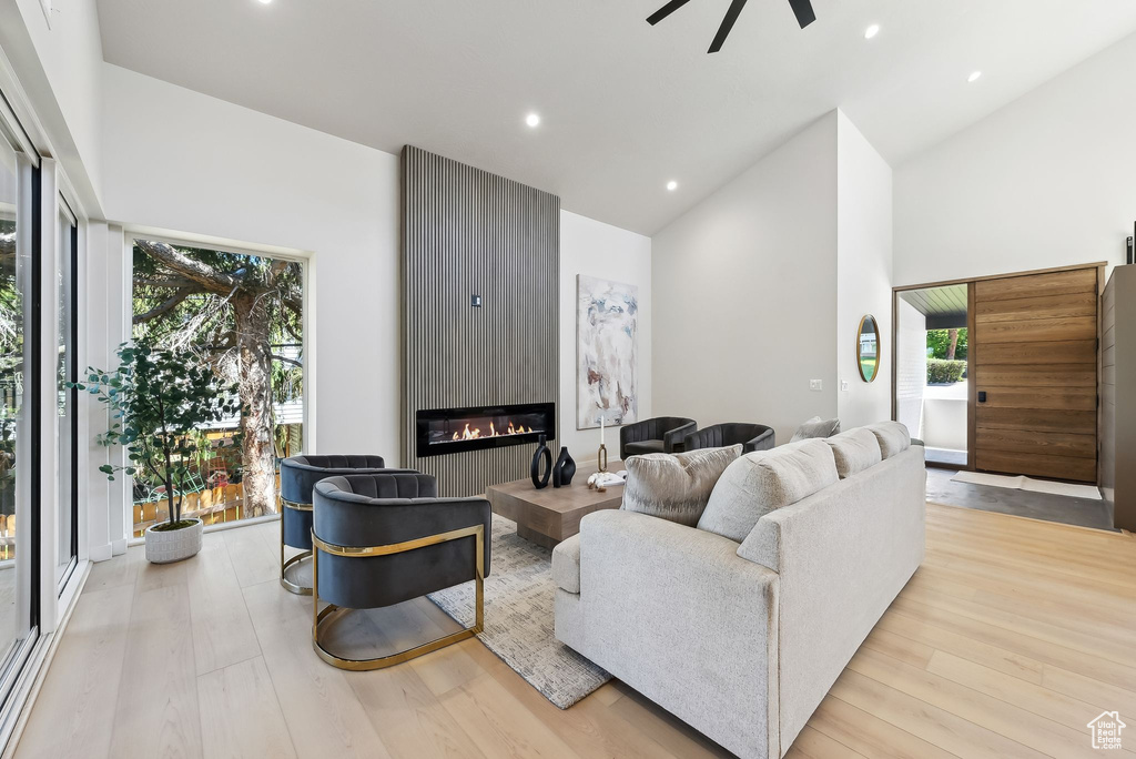 Living area with wood finished floors, high vaulted ceiling, recessed lighting, a large fireplace, and a ceiling fan