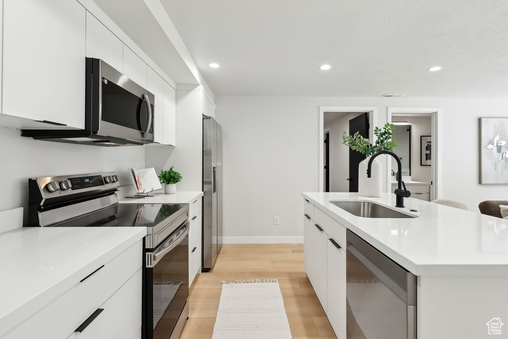 Kitchen with a sink, white cabinetry, modern cabinets, light countertops, and appliances with stainless steel finishes