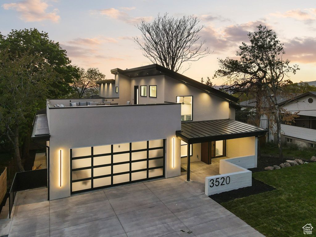 Modern home with driveway, a standing seam roof, metal roof, stucco siding, and a front lawn