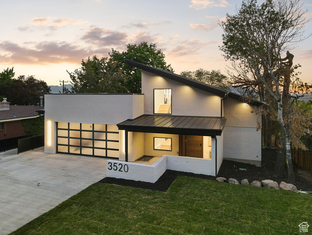 View of front of house featuring stucco siding, metal roof, a lawn, driveway, and a standing seam roof