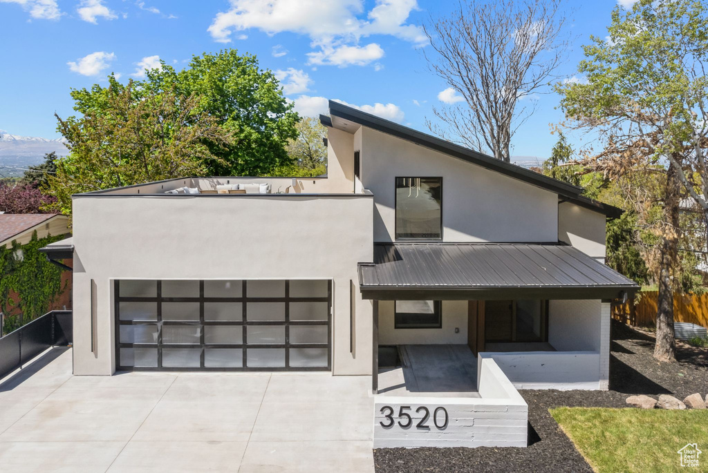 Modern home featuring concrete driveway, stucco siding, metal roof, and a porch