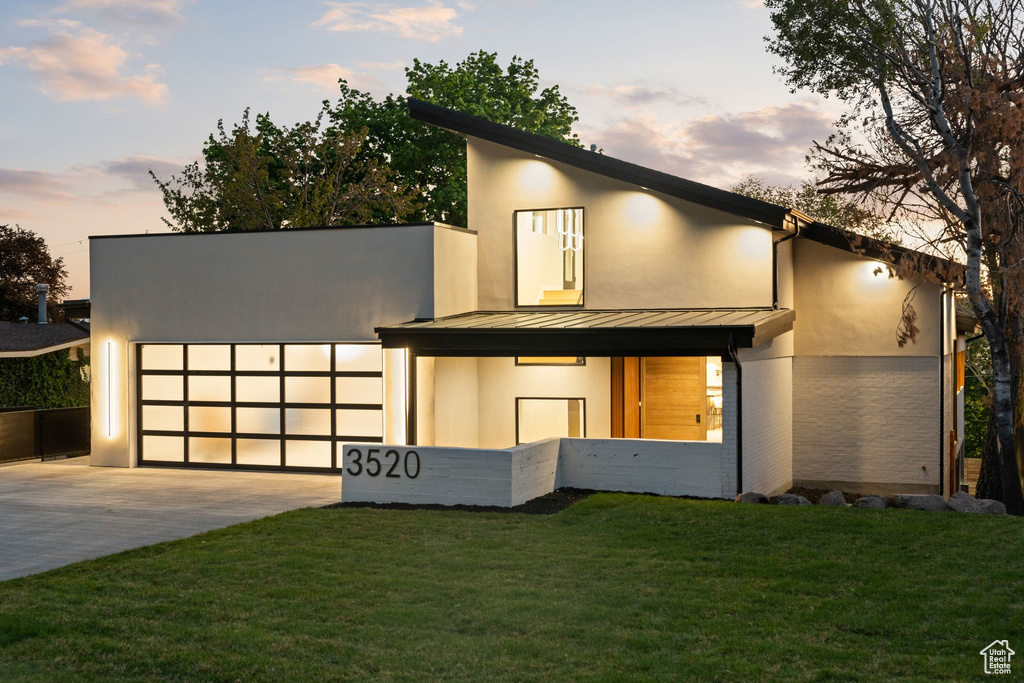 Modern home with a yard, concrete driveway, stucco siding, metal roof, and a standing seam roof