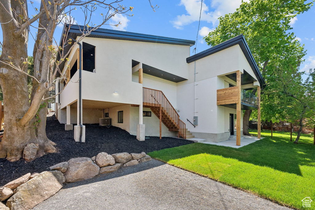 Rear view of property featuring a patio, stucco siding, a lawn, a carport, and central air condition unit